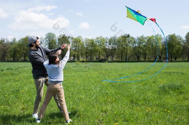 微笑的父亲和女儿飞行的风筝向草地