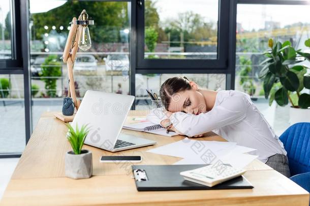 耗尽的年幼的女商人睡眠在她书桌在办公室采用