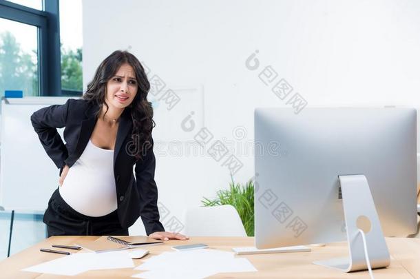 怀孕的女商人和背痛苦在工作场所有样子的