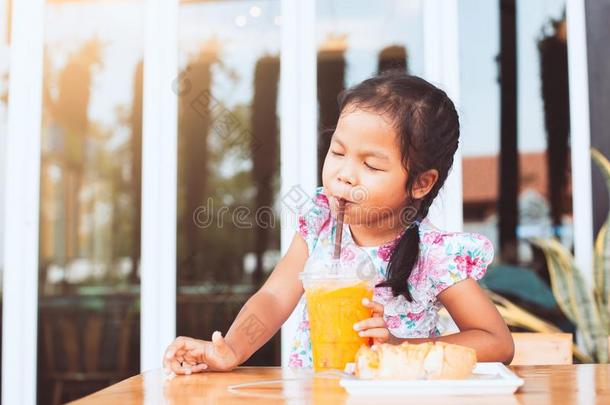 漂亮的亚洲人小的小孩女孩喝饮料桔子果汁