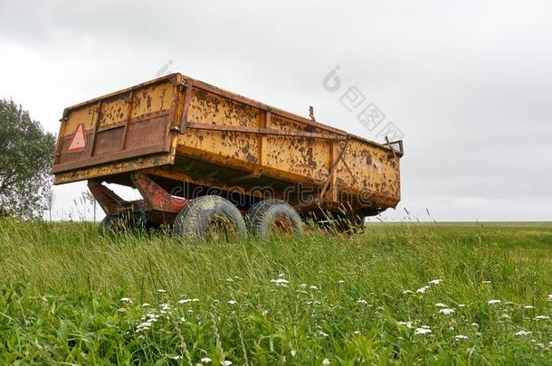 生锈的黄色的农场拖拉机四轮的运货马车采用绿色的风景