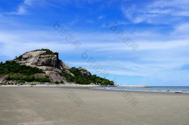 沙的海滩和多岩石的山和蓝色天背景.