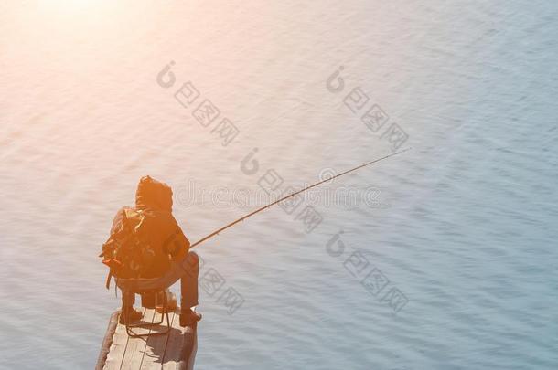 男人和一捕鱼杆坐向指已提到的人岸.阳光
