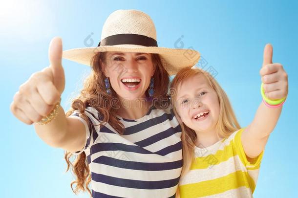 幸福的母亲和女儿展映拇指在上面反对蓝色天