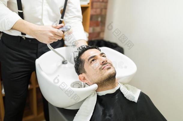 男人获得他的头发洗过的在旁边理发师采用沙龙