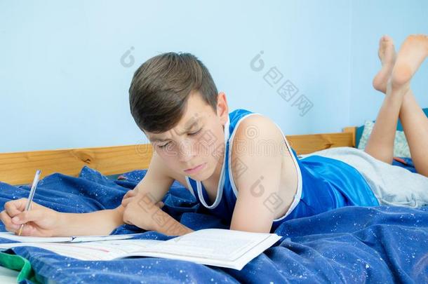 青少年男孩做家庭作业向他的床