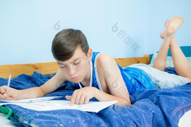 青少年男孩做家庭作业向他的床