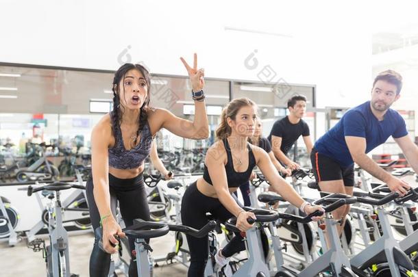 女人做手势胜利在期间锻炼向纺纱自行车采用健身房