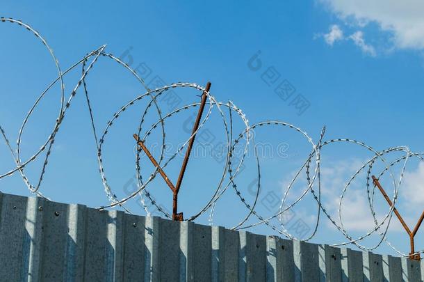 金属栅栏和装有倒钩的金属丝向蓝色天背景