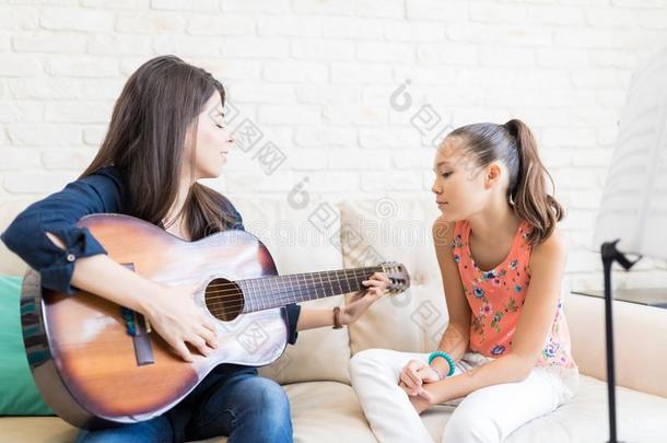 女孩有样子的在教师演奏吉他向沙发