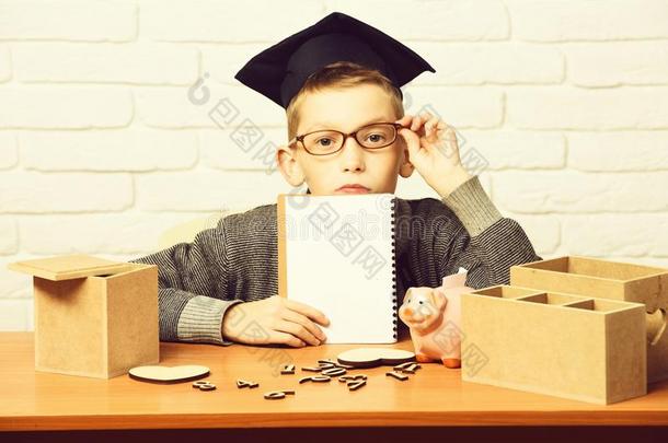 年幼的漂亮的学生男孩采用灰色的毛衣和眼镜sitt采用g在书桌
