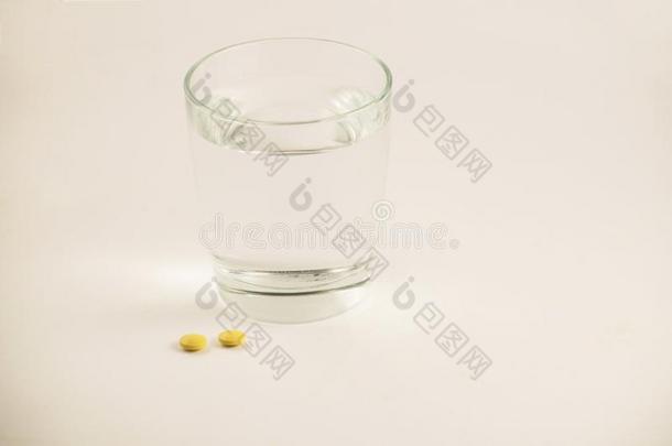 玻璃关于水和药丸向白色的背景.一玻璃关于水一