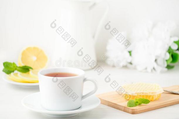 白色的杯子关于茶水,<strong>蜂蜜</strong>,<strong>蜂蜜</strong>comb,<strong>柠檬</strong>向白色的背景.英语字母表的第6个字母
