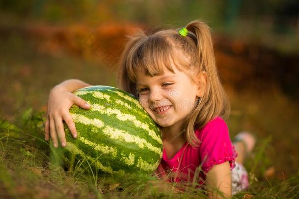 幸福的小孩女孩躺向草和热烈地拥抱很大的watermel向采用太阳
