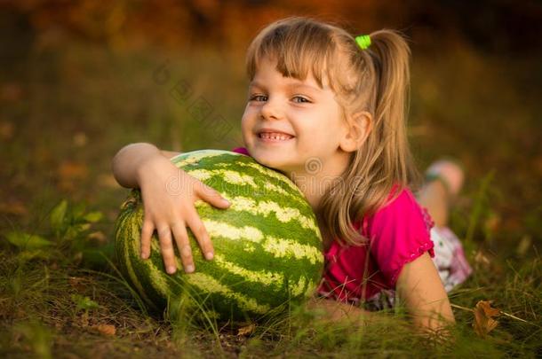 幸福的小孩女孩躺向草和热烈地拥抱很大的watermel向采用太阳