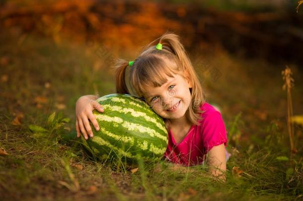 幸福的小孩女孩躺向草和热烈地拥抱很大的watermel向采用太阳