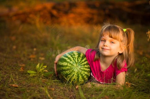 幸福的小孩女孩躺向草和热烈地拥抱很大的watermel向采用太阳