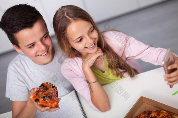 年幼的十几岁的青少年男孩和女孩学习同时-吃意大利薄饼