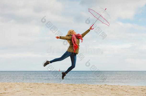 女人用于跳跃的和<strong>透明</strong>的<strong>雨伞</strong>向海滩