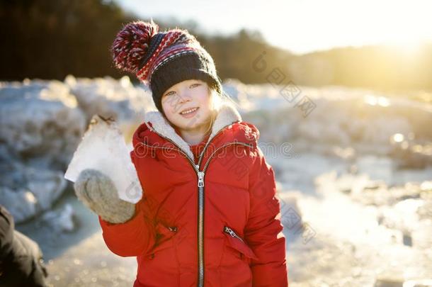 幸福的小的女孩演奏和冰赛跑者起跑时脚底所撑的木块在旁边冷冻的河在的时候