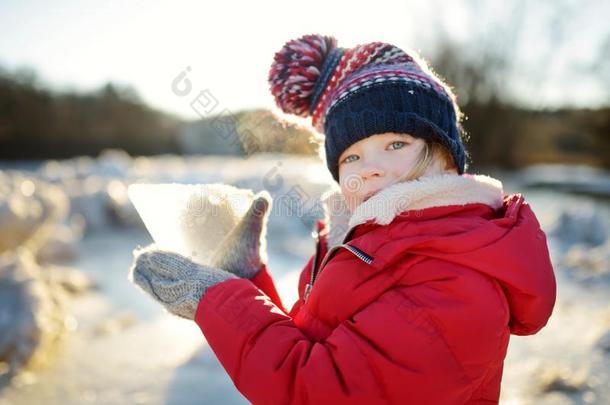 幸福的小的女孩演奏和冰赛跑者起跑时脚底所撑的木块在旁边冷冻的河在的时候