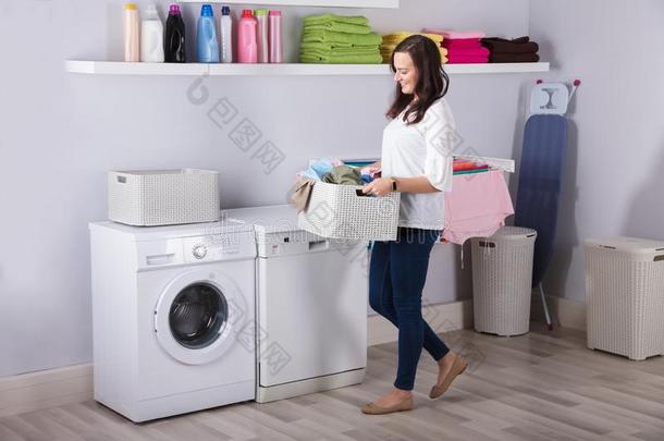 女人起立在近处洗涤机器和篮关于衣服
