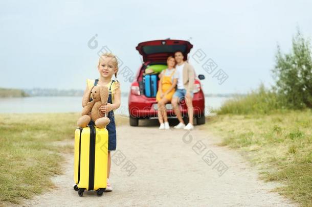 小的女孩和手提箱和玩具兔子在近处汽车向河边