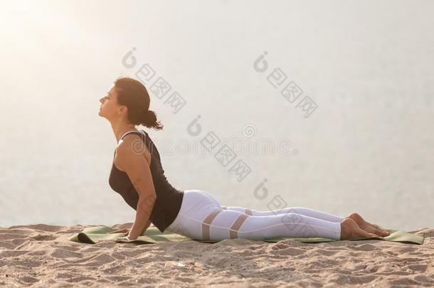 女人开业的瑜伽向指已提到的人海滩.布詹加萨纳,眼镜蛇使摆姿势.oatunit麦片