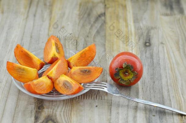 成熟的柿子和盘子和甜的将切开和餐后甜食餐叉向木材