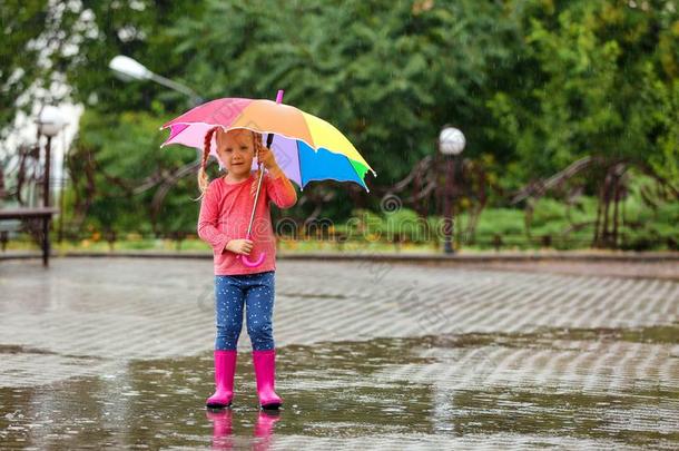 漂亮的小的女孩和明亮的雨伞在下面雨