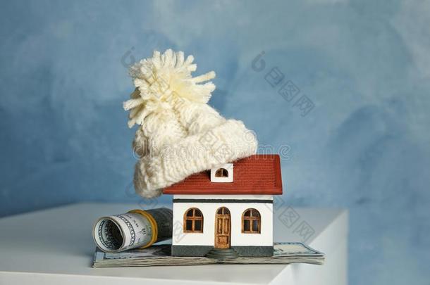 房屋模型和暖和的帽子和钱向表反对颜色后面