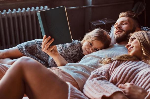 妈妈,爸爸和女儿阅读故事书同时在期间说谎向