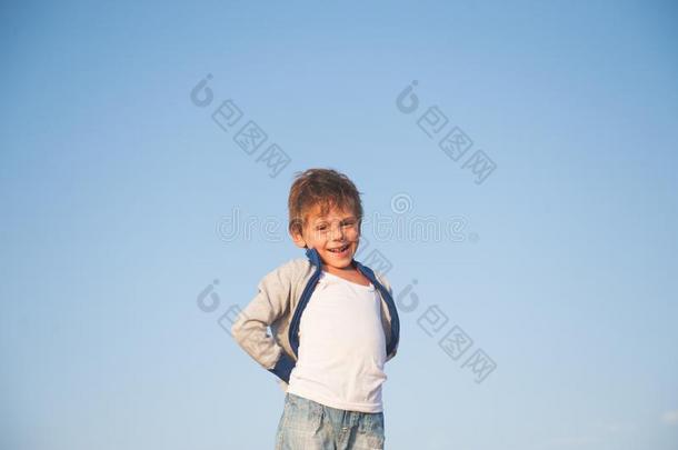 幸福的令人非常高兴的微笑的小的男孩采用毛衣向蓝色天后面