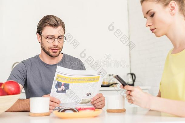 女人使用智能手机和男朋友阅读报纸在表