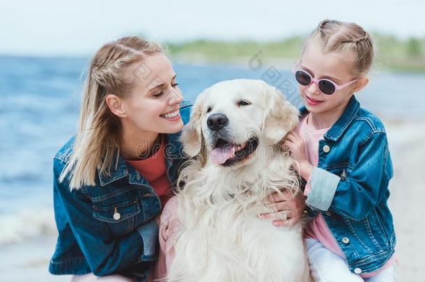 微笑的妈妈和女儿和金色的寻猎物犬狗