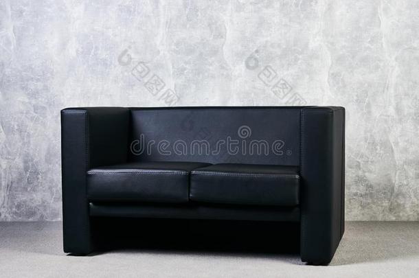 黑的皮沙发反对灰色织地粗糙的墙背景.
