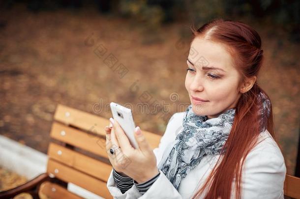 红色的-有毛发的中部-老年的女人和一sm一rtphone采用她h一nd坐