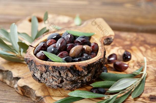 新鲜的棕色的卡拉马塔橄榄和树叶采用橄榄木材碗