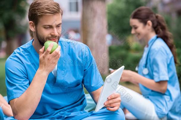 英俊的高加索人医学的学生吃苹果和有样子的