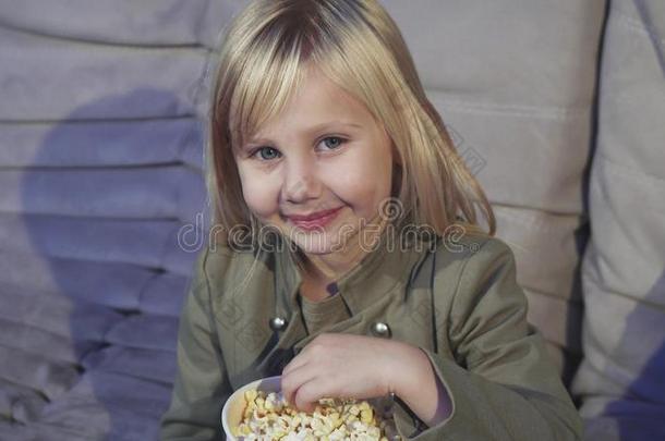 漂亮的小的女孩吃爆米花微笑的向指已提到的人照相机在指已提到的人颈动脉搏动切迹