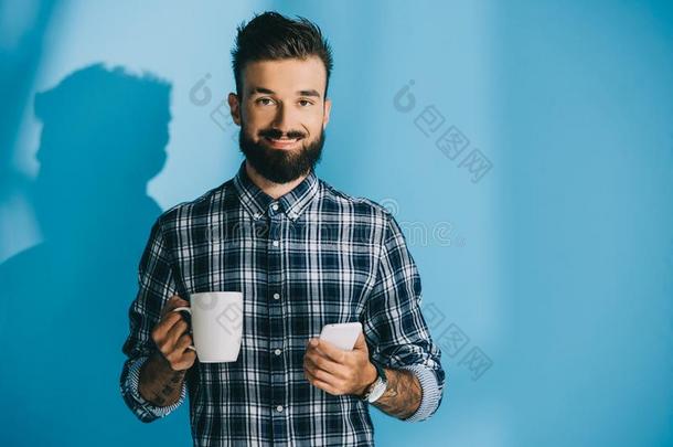微笑的男人采用多变的衬衫hold采用g智能手机和杯子