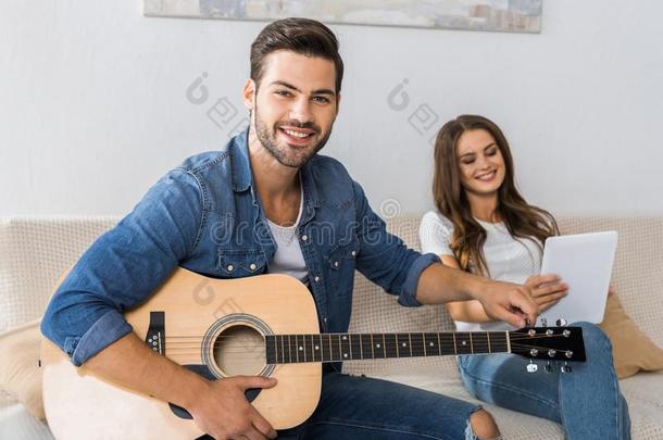 微笑的男人调谐吉他和有样子的在照相机在期间他的女孩