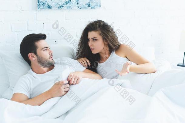年幼的女人争辩和男朋友使用智能手机采用床关于