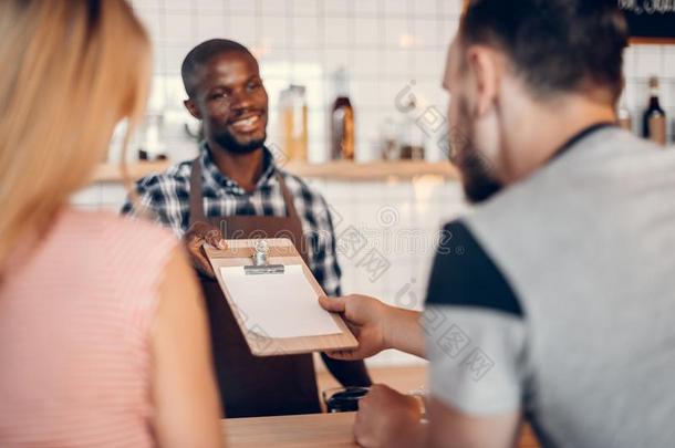 英俊的欢乐的非洲的美国人咖啡馆准备咖啡的员工礼物<strong>菜单</strong>向顾客