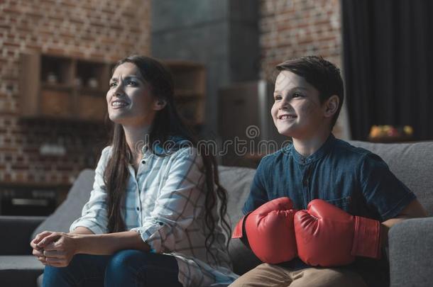 小的男孩采用box采用g拳击手套sitt采用g向长沙发椅和他的母亲和
