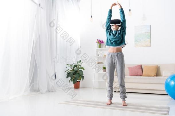 女孩做瑜伽和实质上的现实戴在头上的耳机或听筒向瑜伽席子