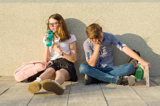 疲倦的少年男女学童坐在近处指已提到的人灰色墙关于指已提到的人school学校