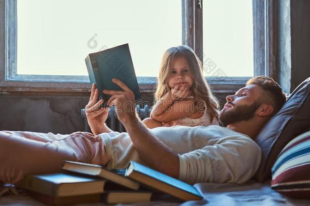 英俊的年幼的父亲阅读故事书他的小的女儿向英语字母表的第2个字母
