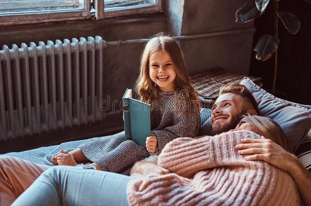 妈妈,爸爸和女儿阅读故事书同时在期间说谎向