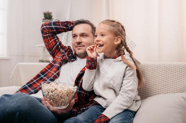 幸福的父亲和女儿吃爆米花和观察television电视机在一起